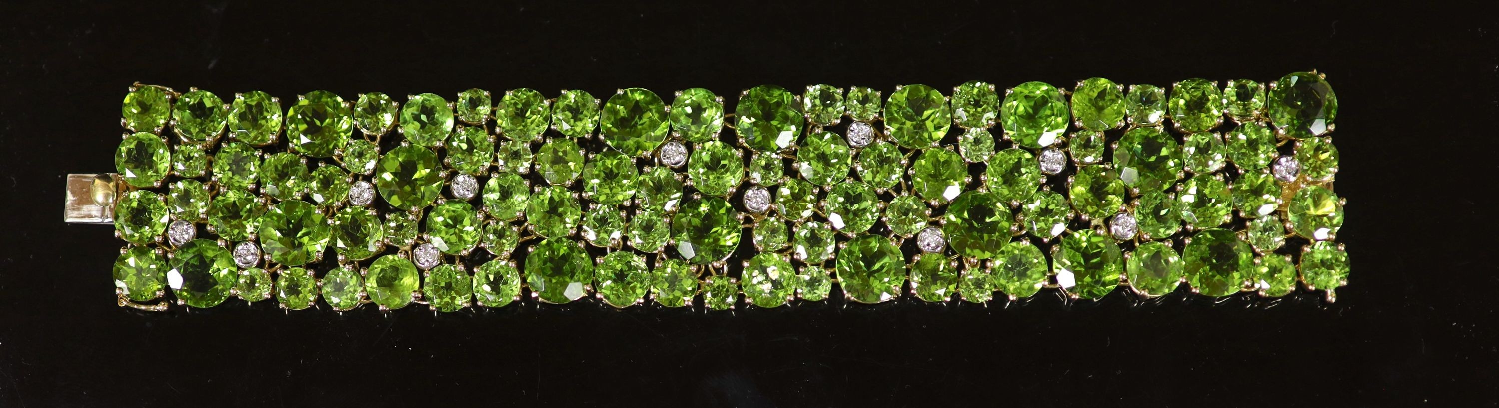 A Continental 18k gold and graduated round cut peridot encrusted bracelet, with twelve stone diamond random set spacers